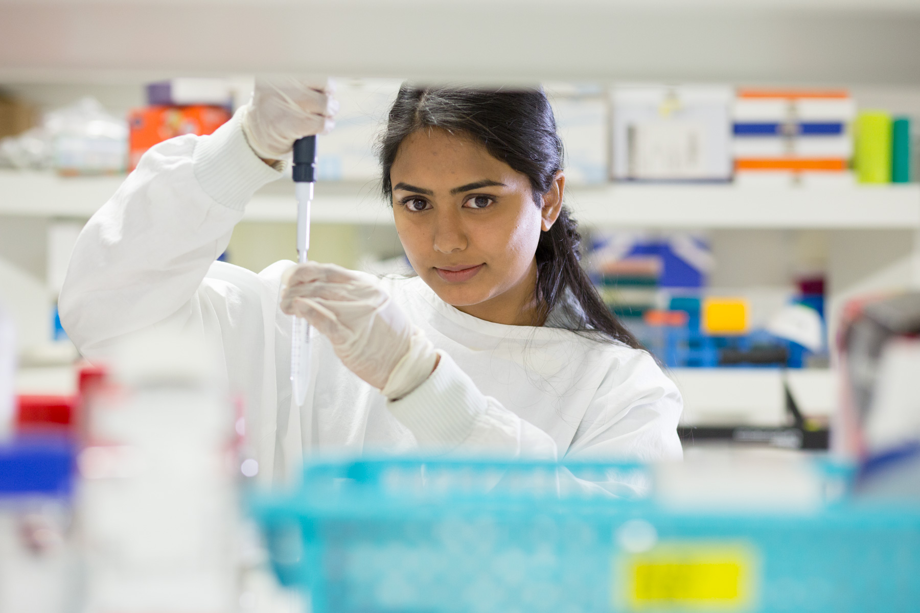 Medical student at work in a laboratory, wearing a white lab coat and blue gloves and using a pipette