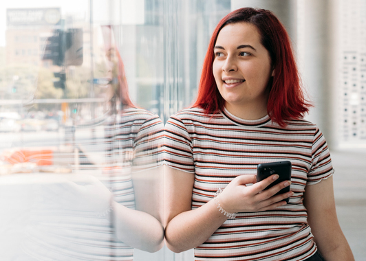 Young woman smiles and holds a mobile phone while glancing away from camera.